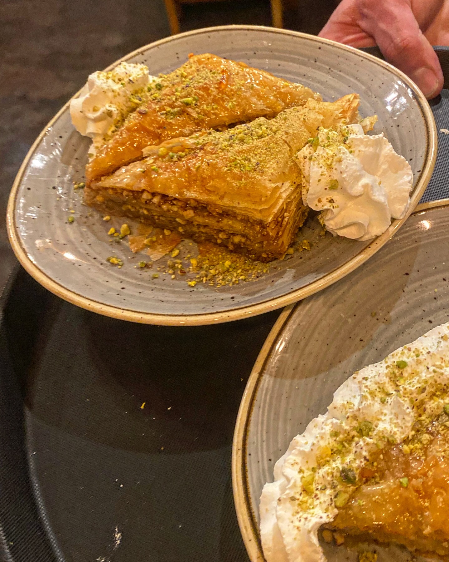 A plate of baklava topped with crushed pistachios and served with whipped cream on the side.