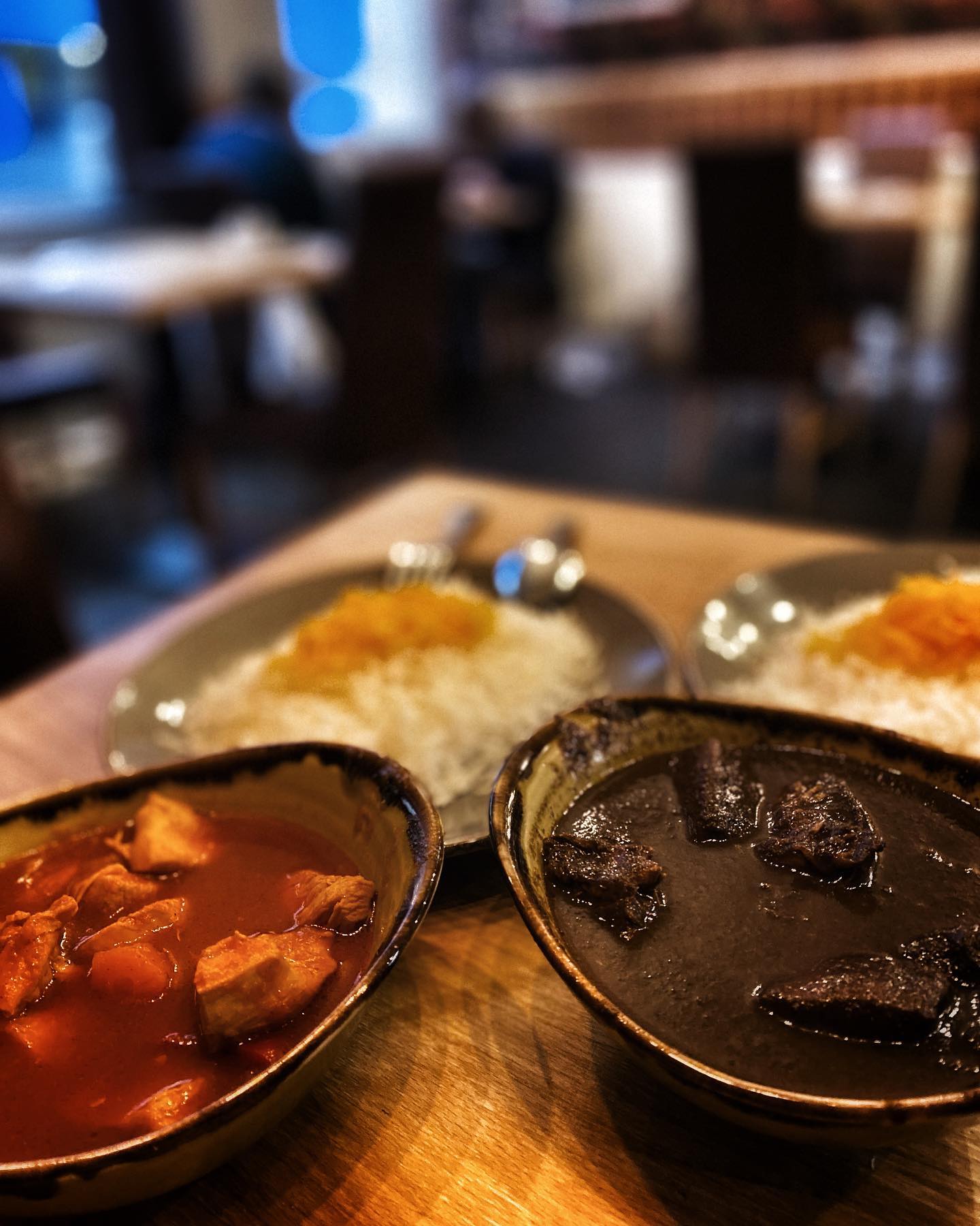 Aromatic Fesenjan served with saffron rice, barberries and vegetables on a patterned plate.